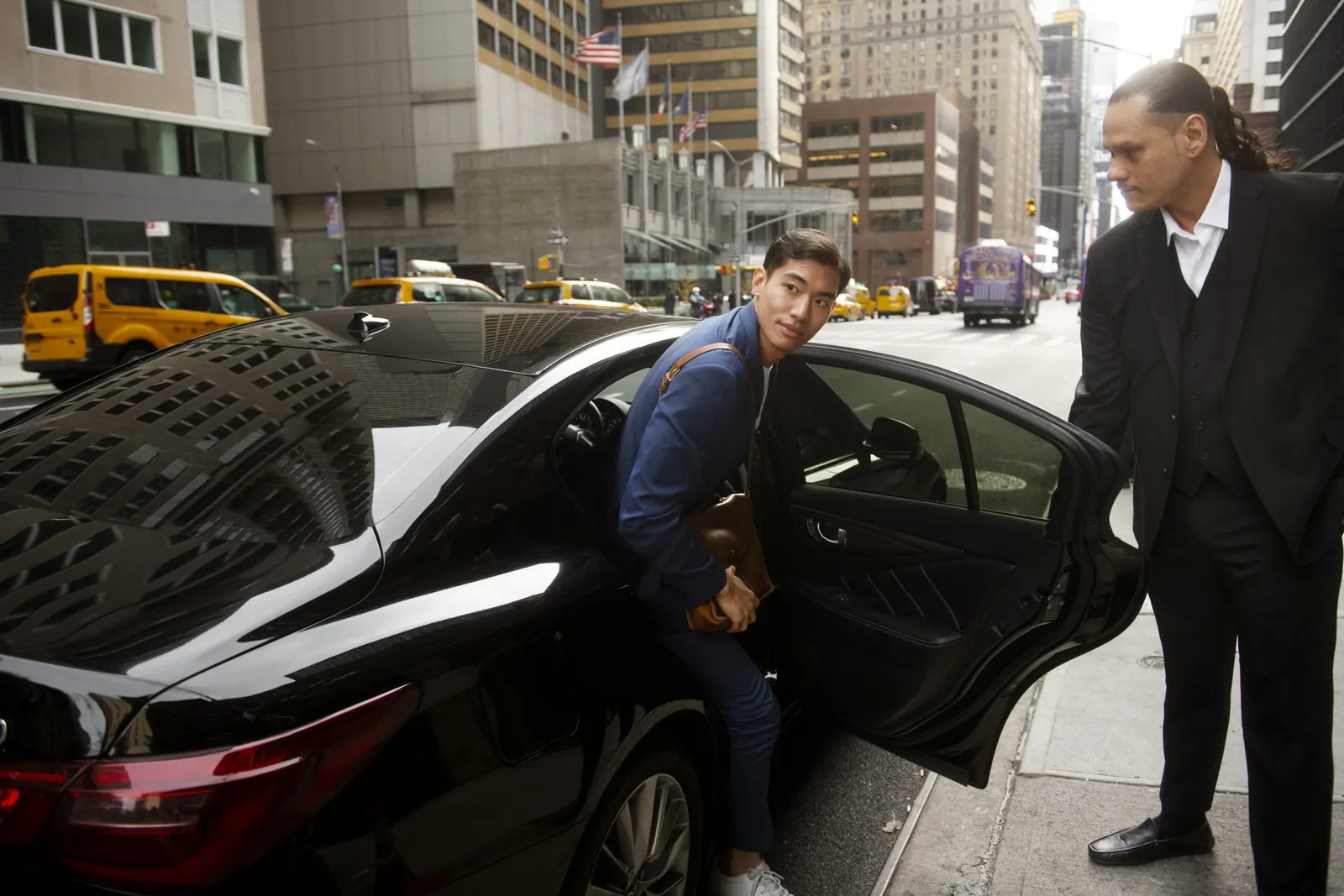 Chauffeur holding open the rear door of a black saloon for a passenger